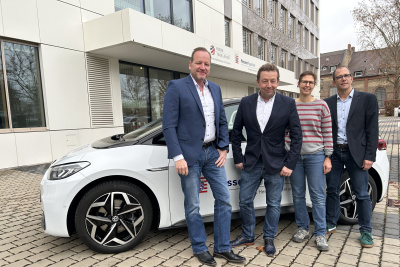 Mitarbeiter der Gesch&auml;ftsstelle Strom bewegt stehend vor einem Elektroauto