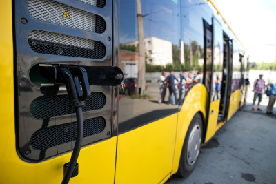 Nutzfahrzeuge - Gelber eBus wird aufgeladen Ein gelber Elektrobus wird aufgeladen, im Hintergrund steigen Personen aus dem Bus.