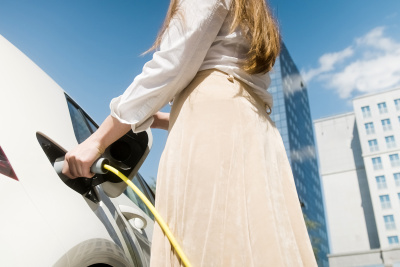 Eine junge Frau lädt ihr Auto während der Arbeitszeit auf einem vom Arbeitgeber bereit gestellten Parkplatz für Elektro-Fahrzeuge auf.